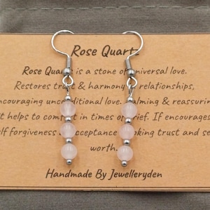 Könnte beinhalten: Ohrringe mit drei hellrosa Rosenquarz-Perlen an silberfarbenen Haken. Auf der Karte steht "Rose Quartz" und "Handmade By Jewelleryden".