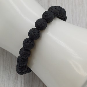 Puede incluir: Un brazalete de cuentas de roca volc&aacute;nica negra. El brazalete est&aacute; hecho de cuentas redondas negras con una superficie rugosa y texturizada.