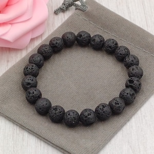 Puede incluir: Un brazalete de cuentas de roca volc&aacute;nica negra sobre un fondo de tela gris.