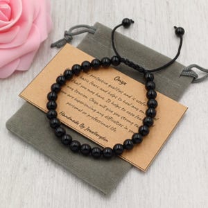 May include: A black onyx bead bracelet with an adjustable black cord, presented on a grey pouch. A small card details the properties of Onyx. The bracelet is handmade by Jewelleryden.