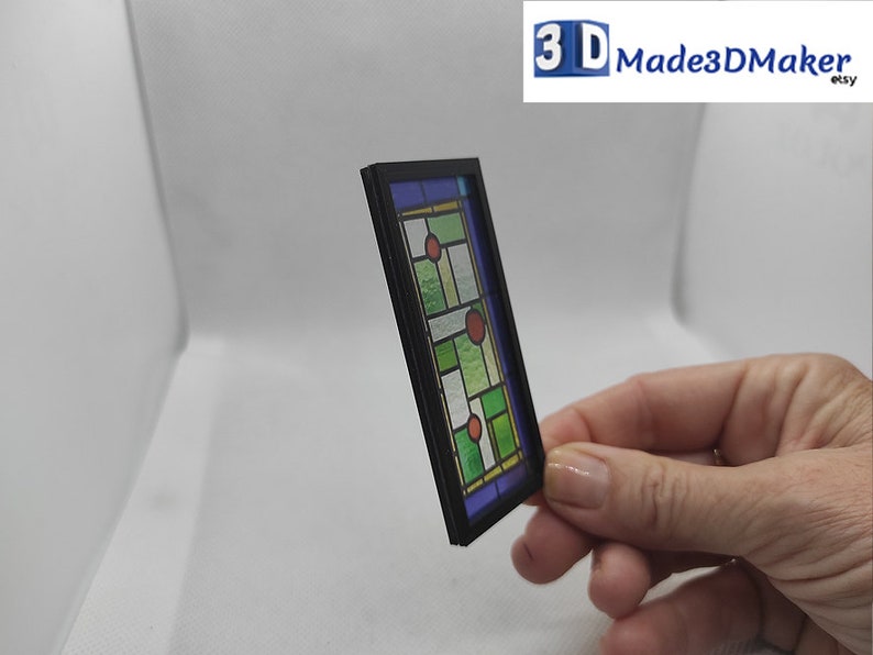 May include: A miniature stained glass window with a black frame. The glass features a geometric design with green, blue, and red accents.