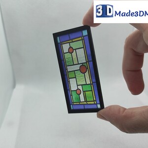 May include: A stained glass window with a black frame. The glass is green, blue, and yellow with red circles. The window is about 4 inches tall.