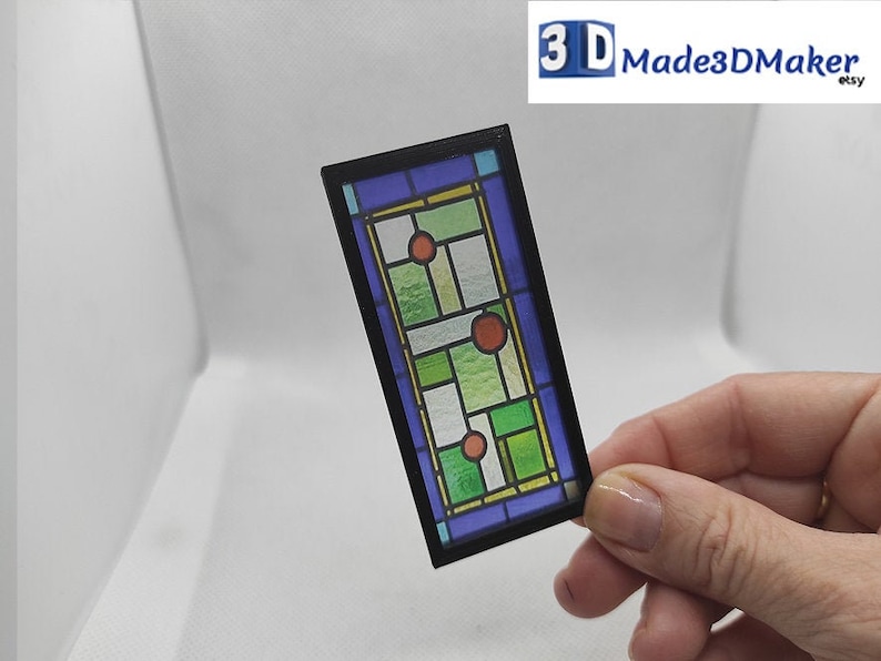 May include: A stained glass window with a geometric design featuring green, blue, and red glass. The window is framed in black and is approximately 4 inches tall.