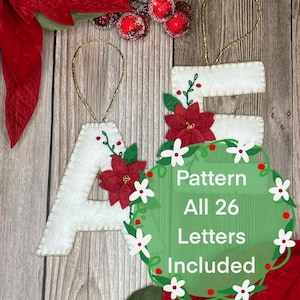 May include: White felt Christmas ornaments in the shape of the letters "A" and "E", each adorned with a red poinsettia and gold hanging string. The image includes a green wreath with text that reads "Pattern All 26 Letters Included".