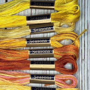 May include: Eight spools of yellow, orange and pink embroidery floss, each labelled "Seasons" with the text "100% Cotton Made in Japan" and the length "8m".