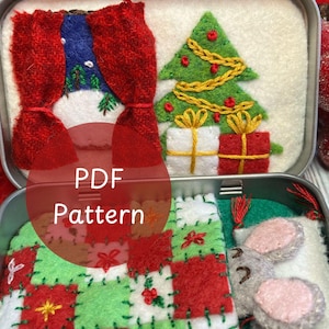 May include: A festive felt Christmas scene in a metal tin. The scene features a red curtain, a green Christmas tree with gold garland, and wrapped gifts. The tin also contains a patchwork quilt and a felt mouse.