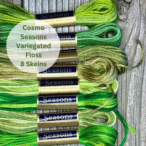 May include: Eight skeins of Cosmo Seasons variegated embroidery floss in various shades of green. Each skein features a gold and navy blue paper label with the text Seasons, 100% Cotton, Made in Japan, and 8M printed on the front.