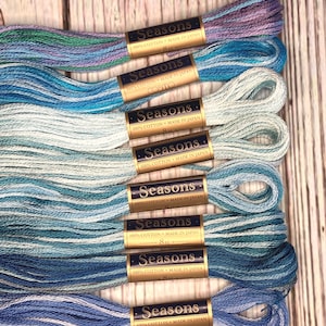 Puede incluir: Ocho carretes de hilo de bordar azul, blanco y verde con la etiqueta "Seasons 100% Algodón Hecho en Japón" en cada carrete.