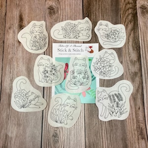 Peut inclure: Plusieurs motifs de broderie sur le thème des chats. Chaque motif représente un chat avec des éléments floraux, imprimé sur un stabilisateur hydrosoluble. Les motifs sont en noir et blanc, avec diverses poses de chats et arrangements floraux.