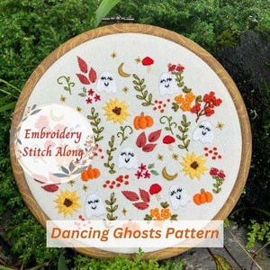 May include: Embroidery hoop with a white fabric background featuring a colorful embroidery pattern of dancing ghosts, autumn leaves, and flowers. The text "Embroidery Stitch Along" and "Dancing Ghosts Pattern" are printed on the hoop.