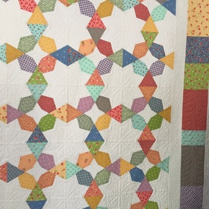 May include: A white quilt with a geometric pattern of colorful fabric squares. The quilt is made up of a repeating pattern of stars and diamonds. The quilt is edged with a border of solid fabric.