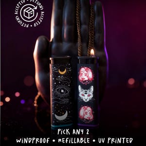 May include: Two black windproof lighters with unique designs. One features celestial symbols, the other has a cat and two women's faces. The text "PICK ANY 2" and "WINDPROOF • REFILLABLE • UV PRINTED" are visible.