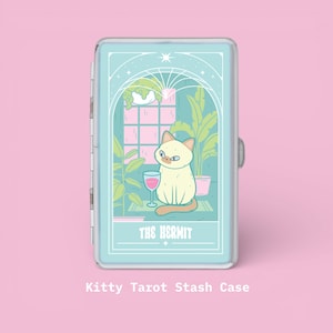 Puede incluir: Un estuche de almacenamiento azul claro con un gato de dibujos animados sosteniendo una copa de vino, con el texto "THE HERMIT". El estuche tiene un borde transparente y un fondo rosa. El texto "Kitty Tarot Stash Case" está en la parte inferior.