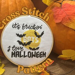 May include: Cross stitch pattern with a white background, black text that says "It's  Trick or Treat", "Bats", and "I love Halloween", and a yellow circle with black bats flying around it.