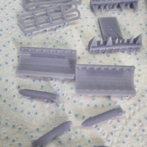 May include: A set of grey plastic model aircraft parts, including a fuselage, wings, tail, and bombs. The parts are on a white surface.