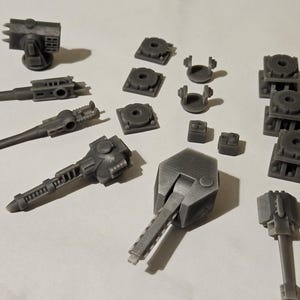 Puede incluir: Un conjunto de cañones en miniatura impresos en 3D y bases para un juego de guerra de mesa. Los cañones son grises y tienen un diseño detallado. Las bases también son grises y tienen una variedad de formas y tamaños.