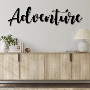 May include: A wooden cabinet with three drawers and a black metal base. The cabinet is decorated with a black metal word art sign that says "Adventure".