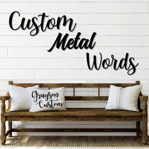 May include: Custom metal words in a cursive font are displayed on a white wall above a wooden bench with two pillows. One pillow has the text "Grayson Custom" printed on it.