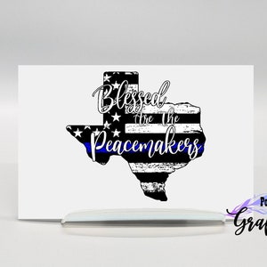 May include: Black and white distressed outline of the state of Texas with a blue line and stars. The text "Blessed are the Peacemakers" is written in white cursive lettering.