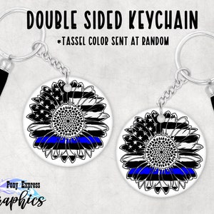 May include: Double-sided keychain featuring a black and white sunflower with a blue line across the center. The sunflower is on a white background. The keychain is silver with a black tassel.