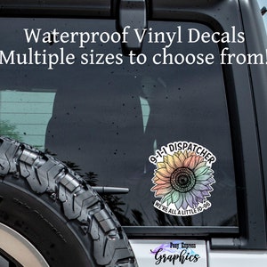 May include: A rainbow-colored sunflower decal with the text "9-1-1 DISPATCHER" and "WE'RE ALL A LITTLE 10-96". The decal is on the back window of a car.