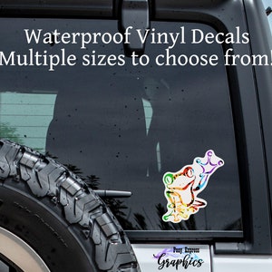 May include: A colorful frog wearing a crown vinyl decal sticker on a black car. The sticker is waterproof and available in multiple sizes. The text "Waterproof Vinyl Decals Multiple sizes to choose from!" is at the top of the image. The text "Pony Express Graphics" is at the bottom of the image.