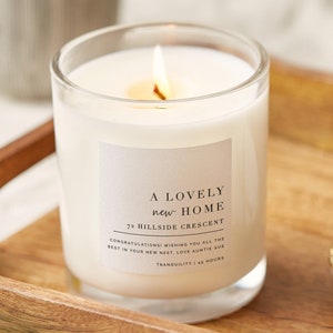 May include: A white candle in a clear glass jar with a label that reads "A Lovely New Home 72 Hillside Crescent Congratulations! Wishing you all the best in your new nest. Love Auntie Sue Tranquility | 48 Hours"
