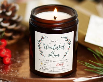 May include: A brown glass candle jar with a white label. The label has a green wreath with red berries and the text "To My Wonderful Mum" with a gold star and the text "From Harit" and "Orange & Cinnamon 25 Hours".