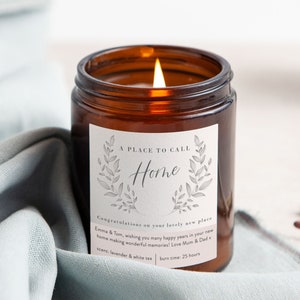 May include: A brown glass candle jar with a white label that reads "A Place To Call Home". The label also includes a floral design and the text "Congratulations on your lovely new place Emma & Tom, wishing you many happy years in your new home making wonderful memories! Love Mum & Dad x scent: lavender & white tea burn time: 25 hours".