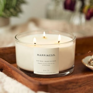 Puede incluir: Un tarro de vela de vidrio transparente con una etiqueta blanca que dice "HAPPINESS. SOY WAX | HAND POURED Bergamot, Lavender, Lemon Tea Tree & Sweet Orange PURE ESSENTIAL OIL BLEND SCENTED CANDLE"