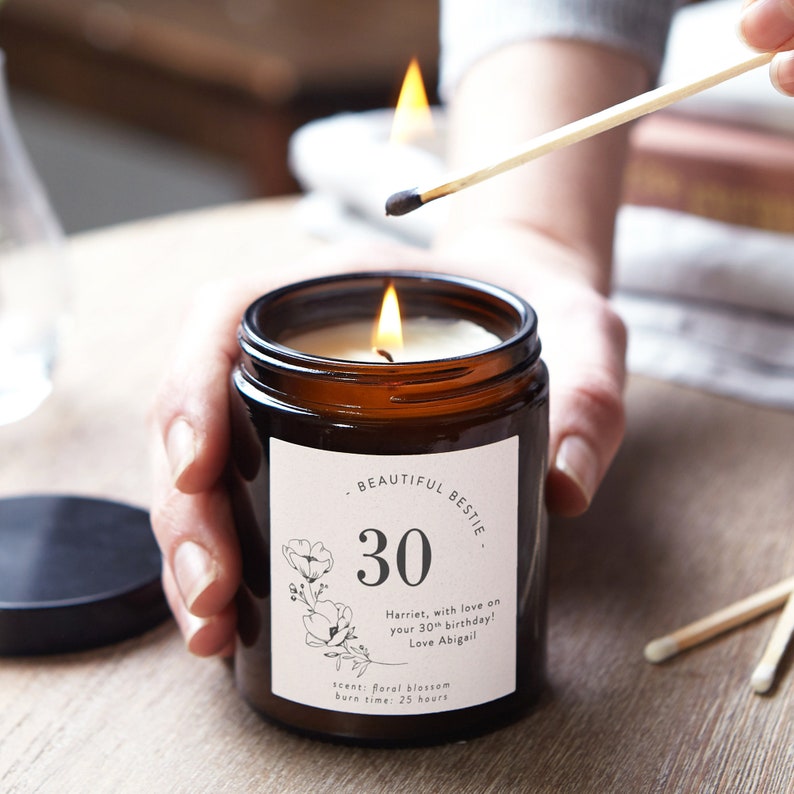 May include: A brown glass candle jar with a white label that says "Beautiful Bestie" and "30". The label also includes a floral design and the text "Harriet, with love on your 30th birthday! Love Abigail", "Scent: Floral blossom", and "Burn time: 25 hours".