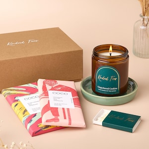 Könnte beinhalten: Ein Geschenkset mit einer braunen Box, zwei Schokoladentafeln mit bunten Designs, einer braunen Glaskerze mit einem grünen Etikett mit der Aufschrift "Kindred Fires Gingerbread Cookies", einem grünen Keramikuntersetzer und einer Schachtel Streichhölzern mit einem grünen Etikett mit der Aufschrift "Kindred Fires".