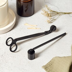 May include: Black candle wick trimmer and snuffer tools. The trimmer has a scissor-like design and the snuffer has a long handle and a round metal cap.