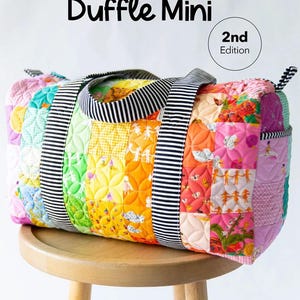 May include: A colorful patchwork duffle bag with a striped handle and accents, resting on a wooden stool. The bag features a variety of quilted fabric squares in rainbow hues. Text on the bag reads "Patchwork Duffle Mini" and "2nd Edition".