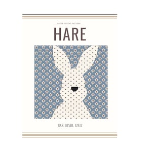 Könnte beinhalten: Papier-Patchwork-Muster für einen Hasen, mit einer weißen Hasensilhouette auf blauem Hintergrund mit weißen Blumen. Das Muster ist in den Größen 20x20, 25x25 und 30x30 cm erhältlich.