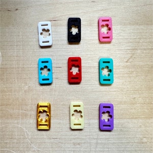 May include: Nine colorful plastic flower-shaped slider buckles in various colors including white, black, red, blue, light blue, pink, gold, cream, and purple.