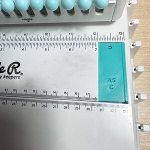 Pode incluir: Uma r&eacute;gua de pl&aacute;stico azul turquesa com o n&uacute;mero "15" impresso nela. A r&eacute;gua tem 32 cm de comprimento e tem um furo no canto superior esquerdo.