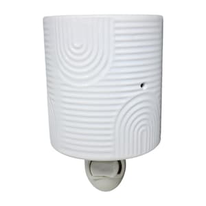 May include: A white ceramic plug-in night light with a geometric design. The cylindrical body features a pattern of curved lines and semi-circles. The base is a silver-colored plug.