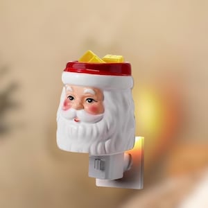 May include: A ceramic Santa Claus night light with a red hat and white beard. The night light has a plug-in base and a small opening at the top. The Santa face has rosy cheeks and a smiling expression. The night light is designed for Christmas.