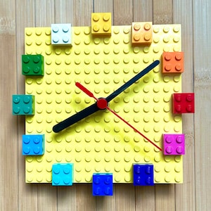Może przedstawiać: Ż&oacute;łty zegar Lego z czarną i czerwoną wskaz&oacute;wką. Tarcza zegara jest wykonana z klock&oacute;w Lego i ma r&oacute;żne kolorowe klocki wok&oacute;ł krawędzi.