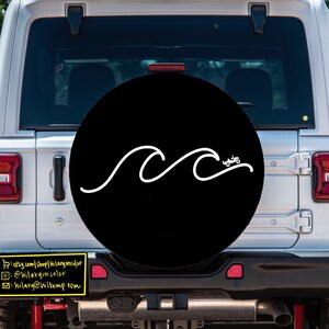 Puede incluir: Un Jeep blanco con una cubierta de rueda de repuesto negra que presenta un dise&ntilde;o de onda blanca. La cubierta de la rueda de repuesto tiene el texto "hilarywilkemp.com".