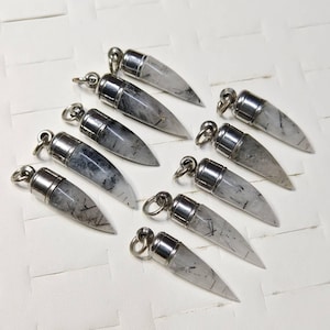 May include: Ten silver pendants with clear quartz crystals and black tourmaline inclusions. The pendants are shaped like a pointed tooth or fang.