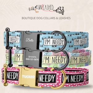 May include: Three dog collars with black and gold buckles. The top collar is light blue with sad eyes and the text I'M NEEDY. The middle collar is multicolored with the text I'M NEEDY. The bottom collar is pink with white hearts and the text I'M NEEDY.
