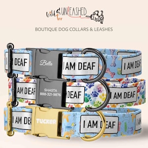May include: Three dog collars with the text "I AM DEAF" on each. The collars have different patterns, including dog illustrations, paw prints, and bones. Each collar has a metal buckle with a name on it.