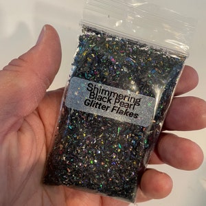 May include: A small clear plastic bag filled with iridescent black glitter flakes. The bag has a label that reads "Shimmering Black Pearl Glitter Flakes".