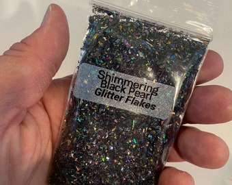 May include: A small clear plastic bag filled with iridescent black glitter flakes. The bag has a label that reads "Shimmering Black Pearl Glitter Flakes".
