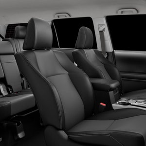 May include: Black leather interior of a car with three rows of seats. The front seats are in the foreground and the back seats are in the background.