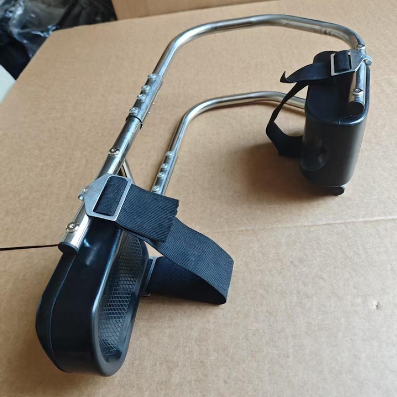 May include: A silver-colored metal medical device with black padded supports and adjustable straps. The device has a curved frame and is designed to provide support. The straps are made of a black, durable fabric.