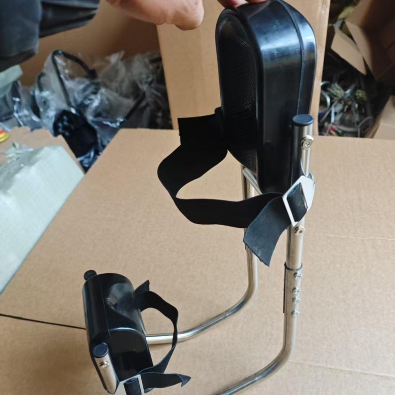 May include: A black and silver medical device with adjustable height. The device has a curved metal frame, black padded supports, and adjustable straps. The device is designed to provide support and stability.