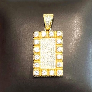 May include: A rectangular gold pendant with a rectangular frame of square-cut, clear stones. The center of the pendant is filled with smaller, clear stones. The pendant is displayed on a black pillow.